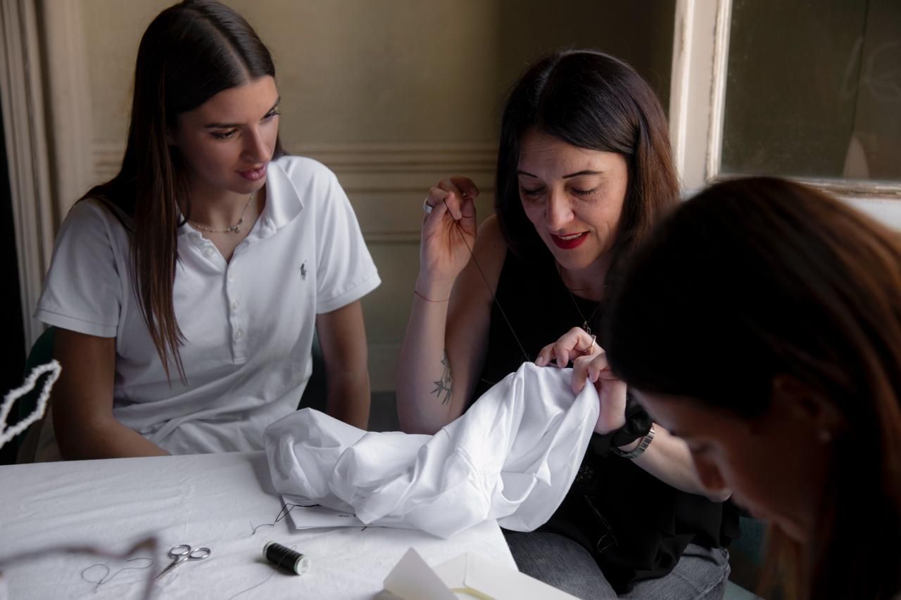 tre donne sedute intorno ad un tavolo ricamano una tela bianca